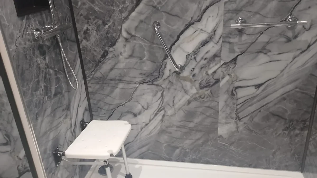 Walk-in shower with grey wall panels, a grab rail and a fold-down seat